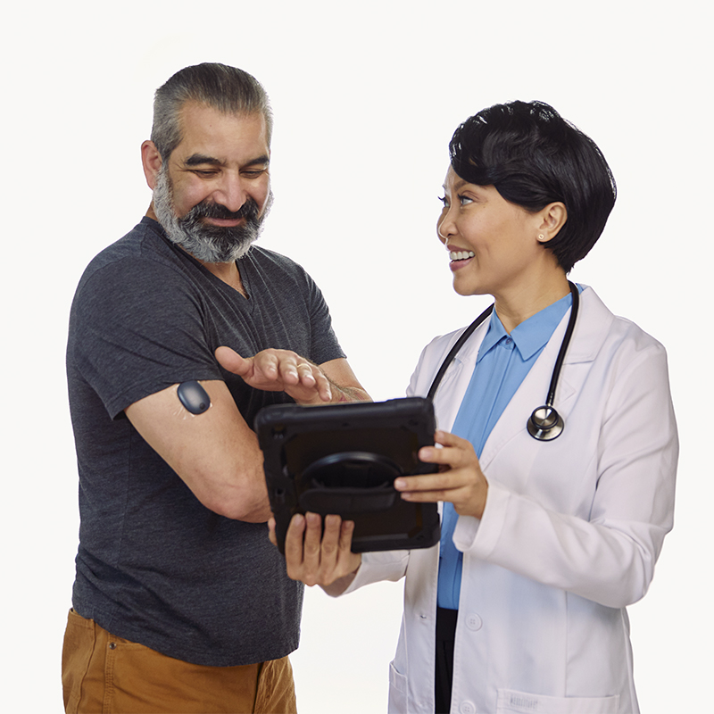 Arzt zeigt einem Patienten, wie er Glukosewerte von einem implantierbaren CGM auf einem Tablet anzeigen kann