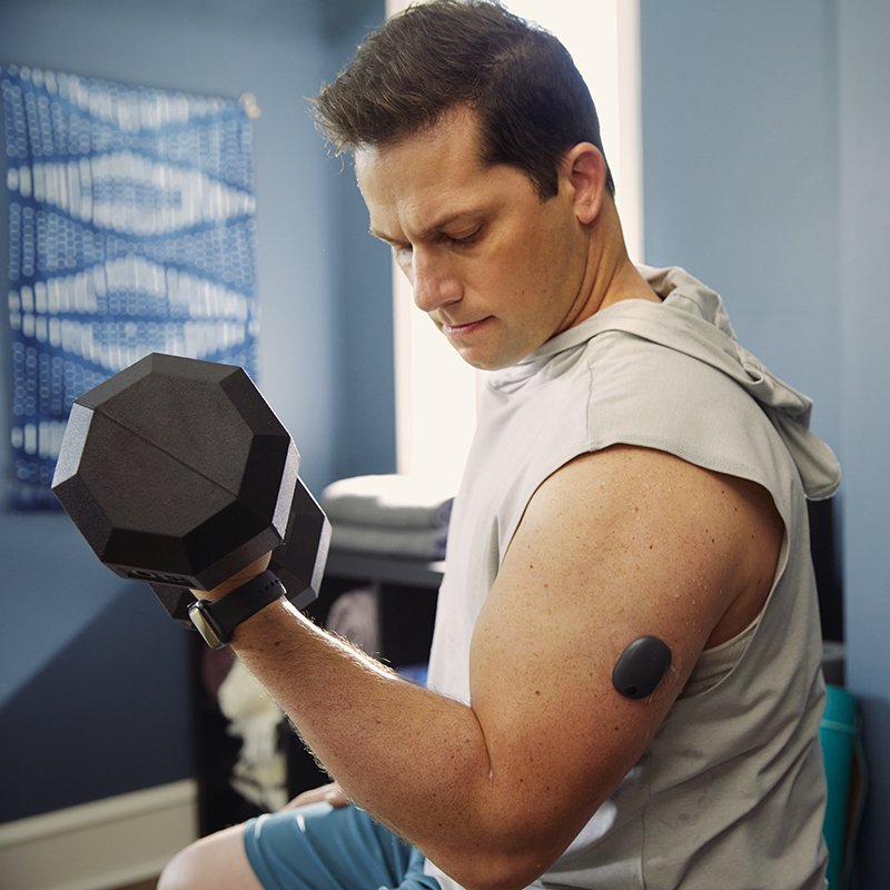 Mann mit CGM-System am Arm stemmt im Fitnessstudio Gewichte